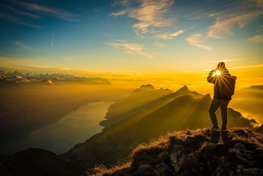 Wanderer steht auf dem Gipfel und fotografiert den goldenen Sonnenuntergang