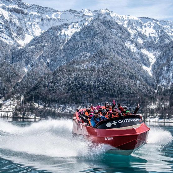 Jetboat unterwegs auf dem spiegelglatten Brienzersee im Winter mit verschneiten Wälder und Bergen