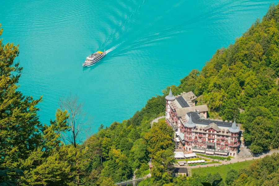 Ein Schiff auf dem türkisen Brienzersee und im grünen Wald das Grandhotel Giessbach