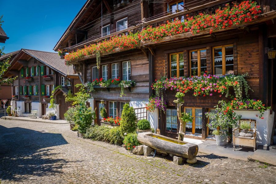Ein mit Blumen geschmücktes Chalet und davor ein handgeschnitzer Brunnen
