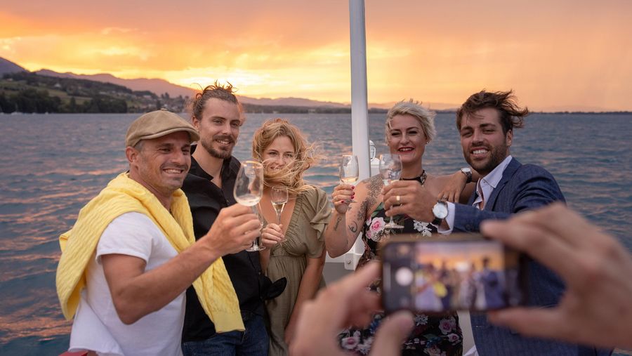 Eine Gruppe erhebt die Gläser und lässt sich mit dem Sonnenuntergang fotografieren.